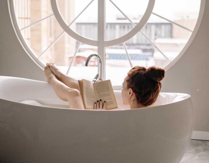 A photograph of a woman in a bath reading a book